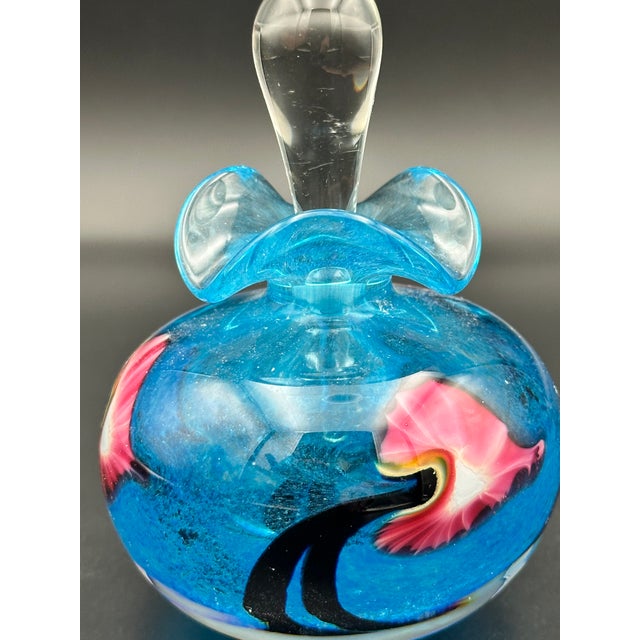 A beautifully hand‑blown studio art glass perfume bottle, featuring a rounded, weighty base with swirling blue coloration...