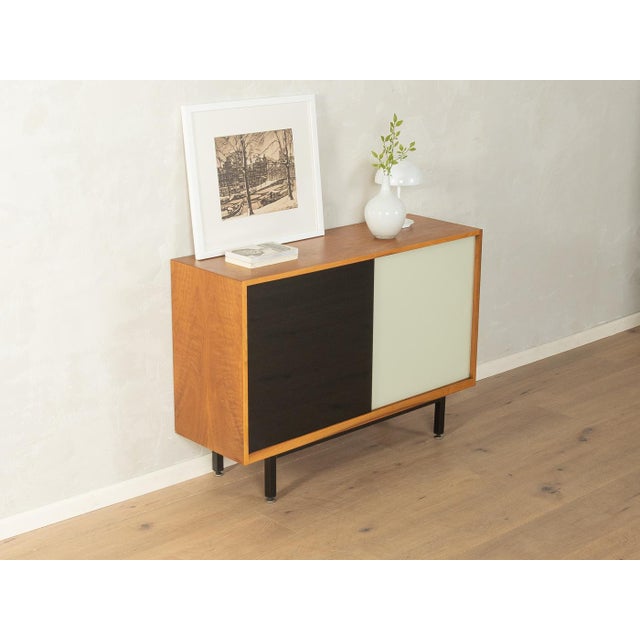 Classic chest of drawers from the 1950s. Walnut veneer body with two black and cream-white glass sliding doors, one shelf,...
