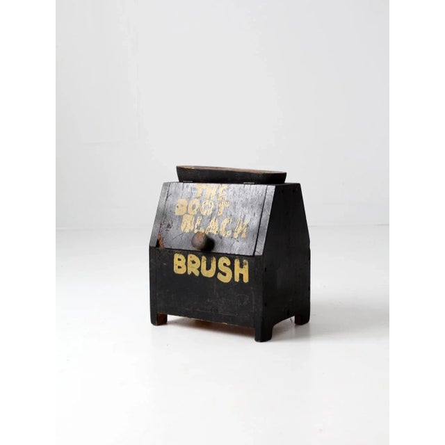 Antique hand-crafted shoe shine box in rustic black wood, featuring the hand-painted inscription “The Boot Black Brush” in...