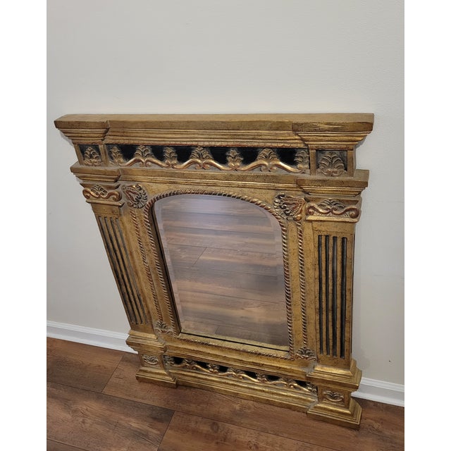 Ornate gilt wood wall mirror with an arched frame and carved decorative elements. The frame features reeded columns with...