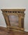 Ornate gilt wood wall mirror with an arched frame and carved decorative elements. The frame features reeded columns with...