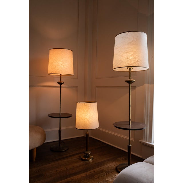 A sculptural mid-century floor lamp that pairs light with a place to set things down. A weighted, patinated metal base...