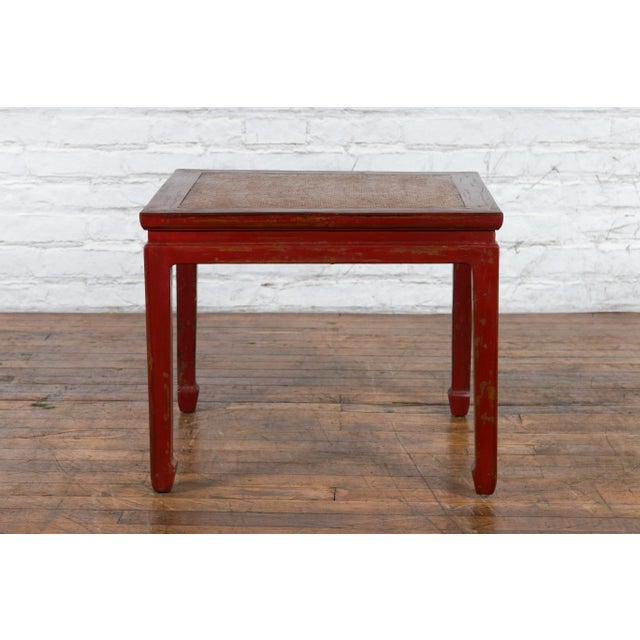 A Chinese Qing Dynasty period side table from the 19th century, with red lacquer, woven rattan top, horse hoof legs and...