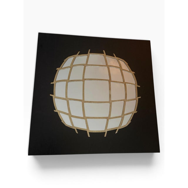 Striking modern wall sculpture featuring a large mirrored globe form framed by a dimensional gold-tone grid, mounted...