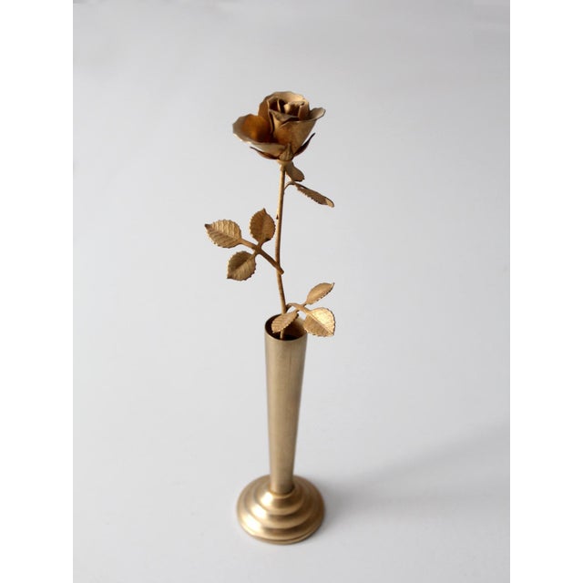Vintage brass rose sculpture in a slender bud vase, offering a warm glow and elegant Hollywood Regency style. The detailed...