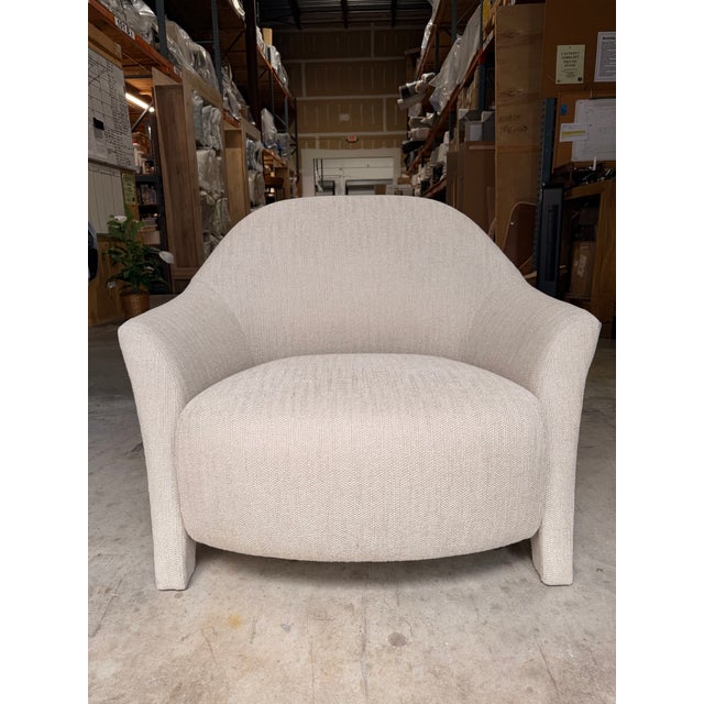 Contemporary barrel lounge chair featuring a sculptural silhouette upholstered in a soft ivory textured fabric for a warm,...