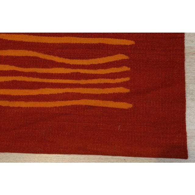 This red and rust wool rug features a sturdy flat weave construction in the Kilim style. The primary color palette...