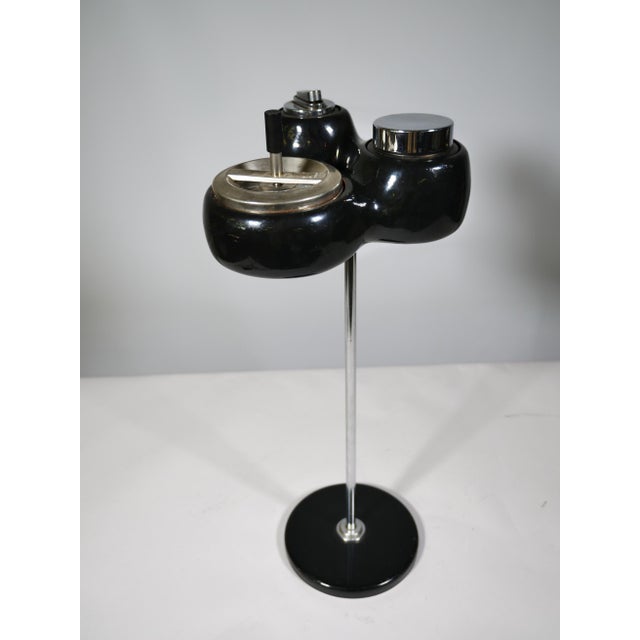 Standing ashtray in a space-age design, made of plastic and metal, with an integrated cigarette dispenser and lighter....