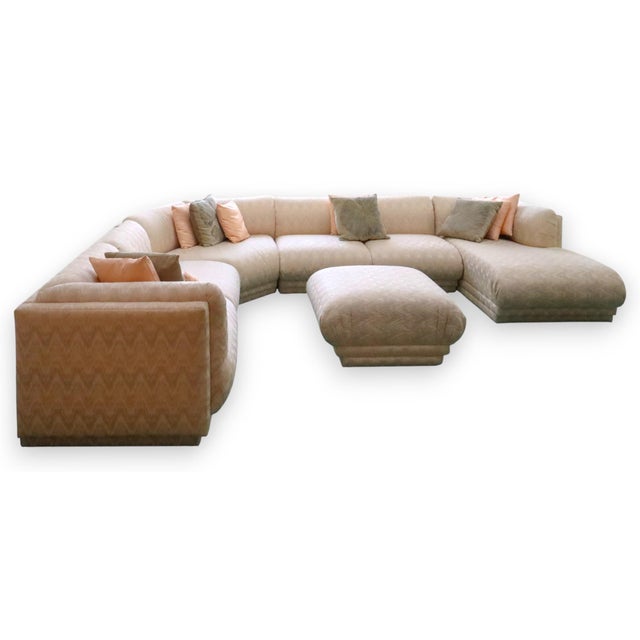 Vintage sectional sofa upholstered in a soft blush pink textured fabric. The sofa features a curved corner configuration...