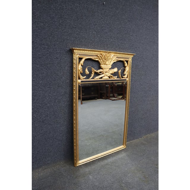 Louis XVI style rectangular mirror with an ornate giltwood frame featuring a central acanthus leaf urn, crossed rifles,...