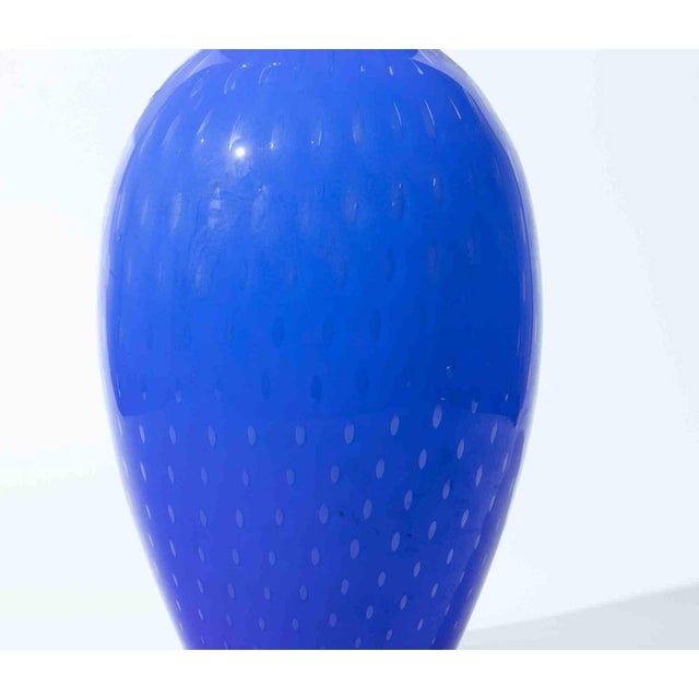 Striking hand-blown art glass vase in a vibrant cobalt blue tone, featuring a delicate all-over polka dot pattern. The...