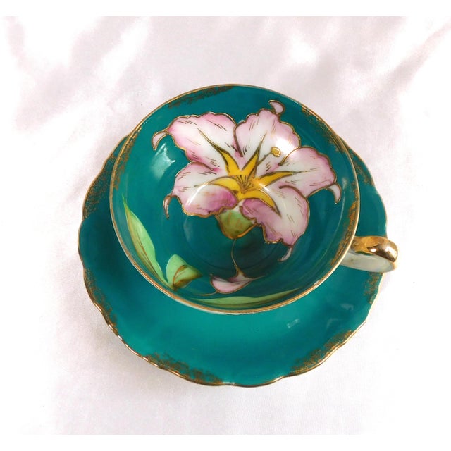 This is a teal color footed teacup and matching saucer with gold trim and a large pink flower outlined in gold. The flower...