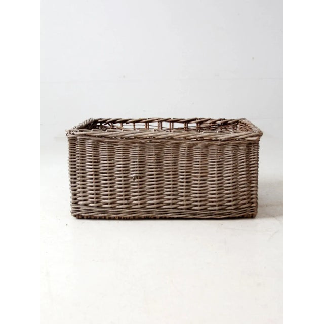 This antique wicker basket features a rectangular form with rich, handwoven texture and a braided rim that adds subtle...