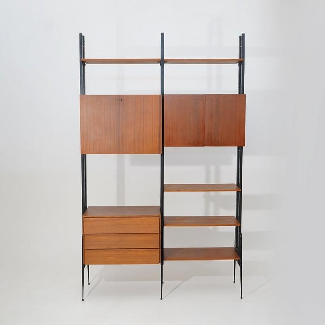 Italian modular shelving system from the 1950s, defined by vertical wooden uprights supporting suspended storage units and...