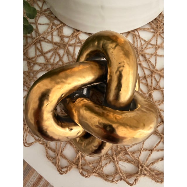 Contemporary sculptural gold knot decorative object featuring an organic hammered metallic finish. A versatile accent...