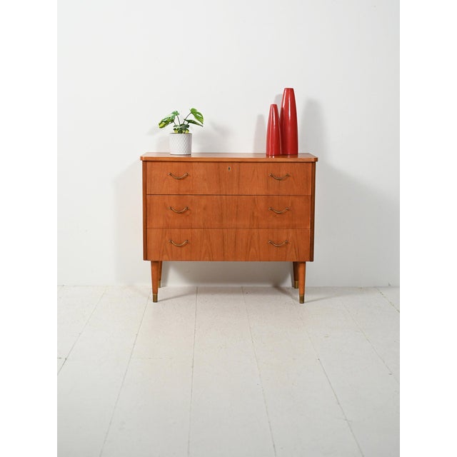 Three teak drawers with flamed grain, brass handles and ferrules: clean lines with a subtle deco accent. A compact and...