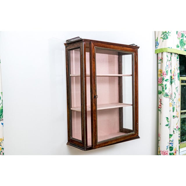 A small antique English mahogany wall-hanging three-sided glass vitrine display cabinet with reddish-brown patina, a...
