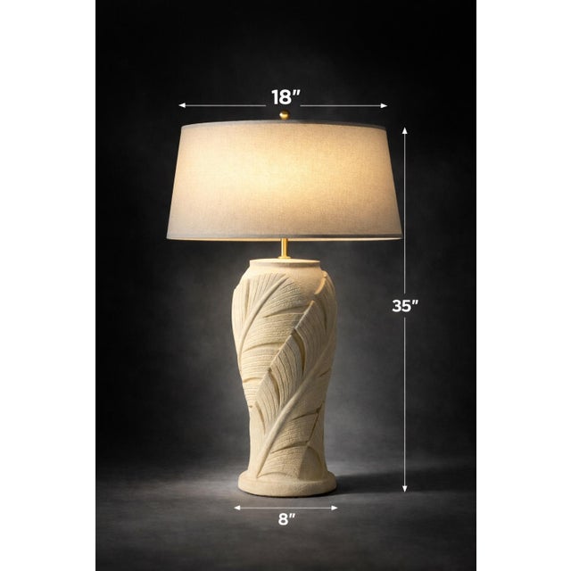 A large sculptural Palm Beach style table lamp featuring dramatic carved leaf relief and an oversized linen shade. With...