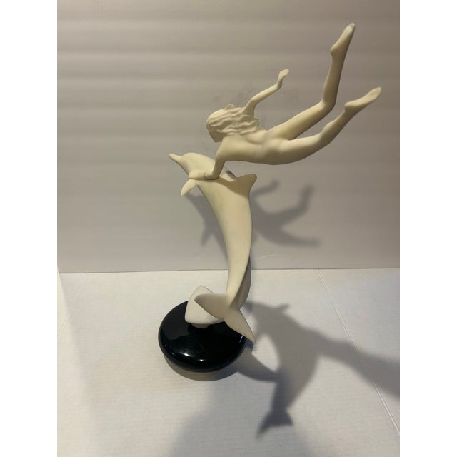 Graceful vintage sculpture captures a nude female poised on top of a dolphin. Soft ivory tone mounted on a contrasting...