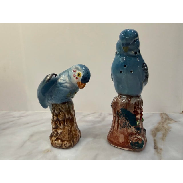A sweet pair of vintage figural salt and pepper shakers modeled as powder blue parakeets perched on tree stumps. One bows...