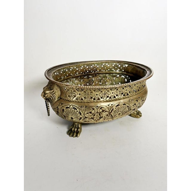 A substantial decorative brass planter, richly adorned with openwork floral motifs, resting on sculpted lion's paws and...