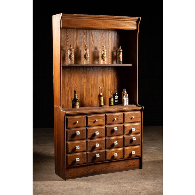 This 1920s apothecary hutch features porcelain drawer pulls labeled with different medicines and medical tools to aid in...