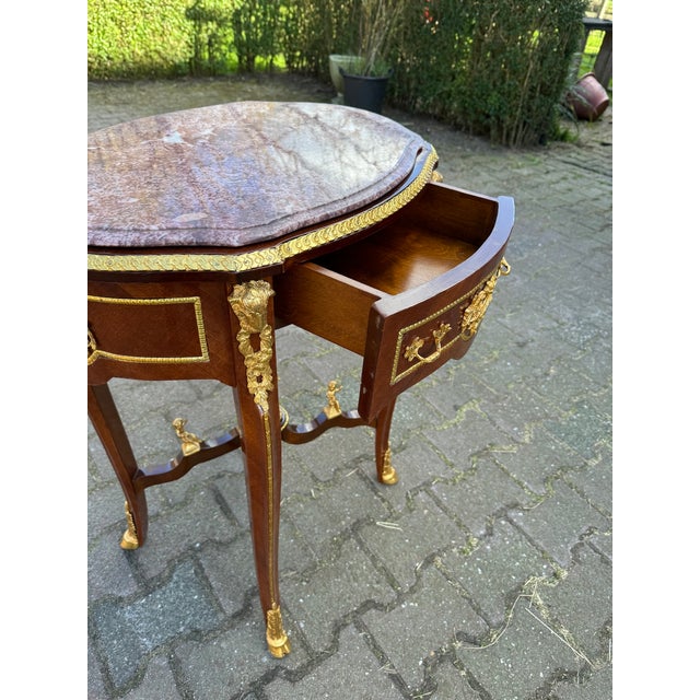 A refined 1960s French Louis XVI–style oval center table, crafted from solid mahogany with gilded bronze accents and an...