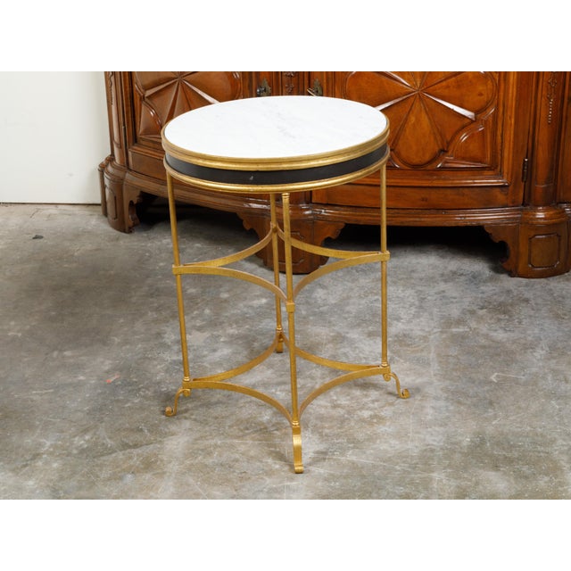 An Italian gilt metal side table from the mid 20th century, with white marble top and in-curving accents. Created in Italy...