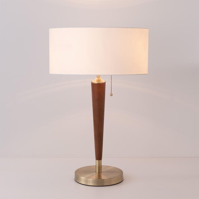 The Pasadena Table Lamp is a modern table lamp with a weathered brass steel body and base, complemented by a white linen...