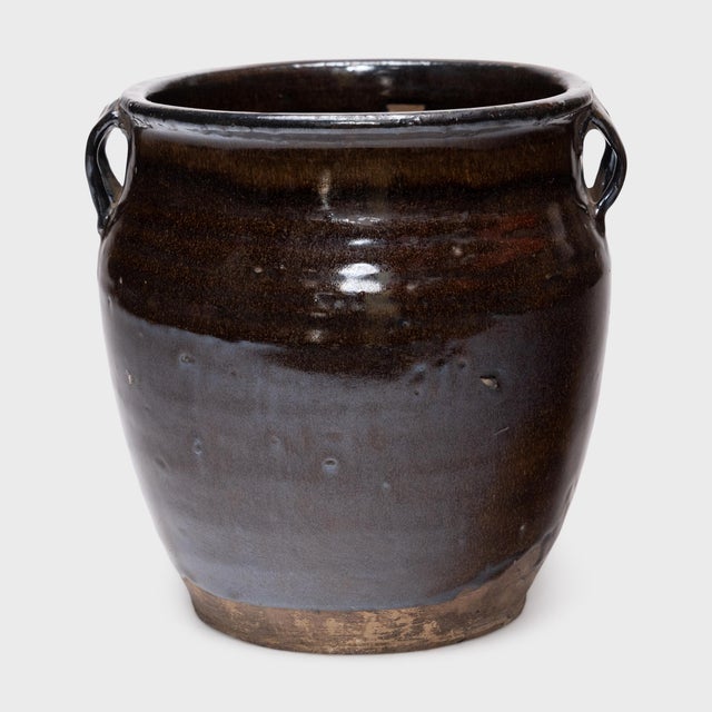 This antique Chinese jar from the early 20th century is cloaked inside and out with a dark brown glaze, shimmering with...