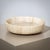 A large stone bowl crafted from beige onyx, featuring a minimalist design. The bowl is characterized by its high rim and...