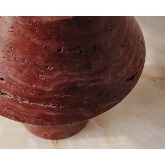 A sculptural table lamp carved from solid red travertine. A softly tapered cylindrical base supports a wide conical shade....