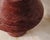 A sculptural table lamp carved from solid red travertine. A softly tapered cylindrical base supports a wide conical shade....