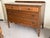 A wooden chest of drawers featuring two upper small drawers with burlwood veneer panels and a central carved rosette...