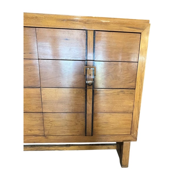 A vintage mid-century chest of drawers with a faux buckle front and eight drawers and with a stretcher base. The drawers...
