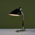 Industrial desk lamp with a black-enameled metal shade. The lamp sits on a rectangular steel base with a curved stem and...