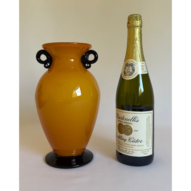 A striking hand-blown art-glass vase featuring a warm ochre-yellow exterior over an opaque white interior. Its full...