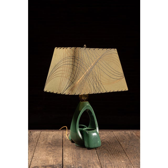 Mid-century modern ceramic table lamp featuring a sculptural open teardrop body finished in a rich glossy green glaze. The...