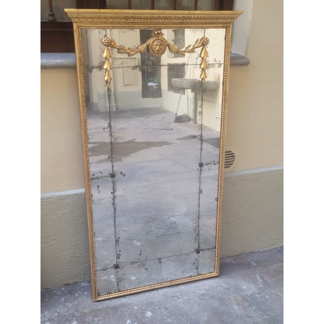 An elegant Louis XVI-style mirror, crafted from finely carved and gilded wood, featuring a rich neoclassical ornamental...