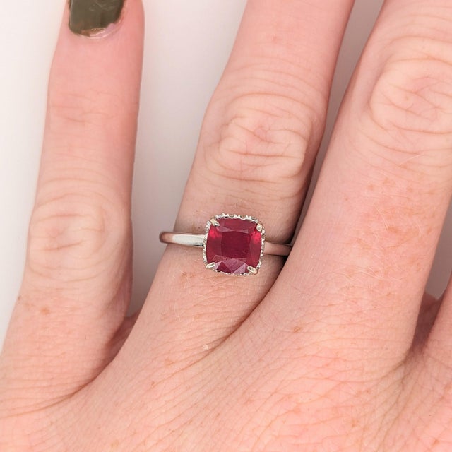 A 1.74ct Madagascar Ruby of vivid character, hand-set in 14K White Gold framed by a Diamond Halo. The cushion stone is cut...