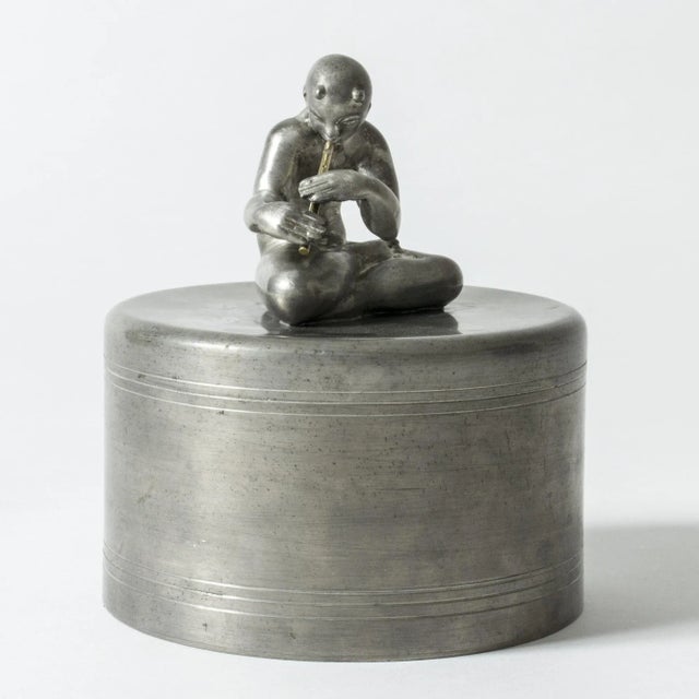 Amazing pewter jar by Nils Fougstedt, adorned with a flute playing, cross-legged Pan figurine. The tiny flute is made from...