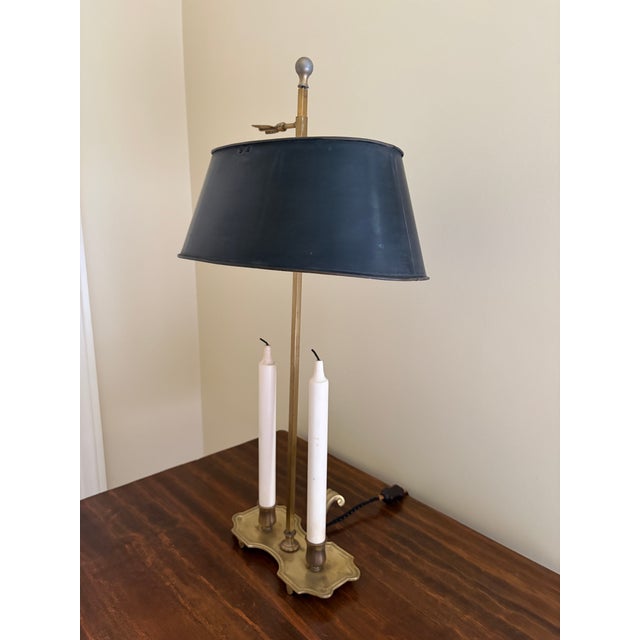 A classic bouillotte lamp rendered in warm brass, distinguished by its clean, tailored black tole shade. The form traces...