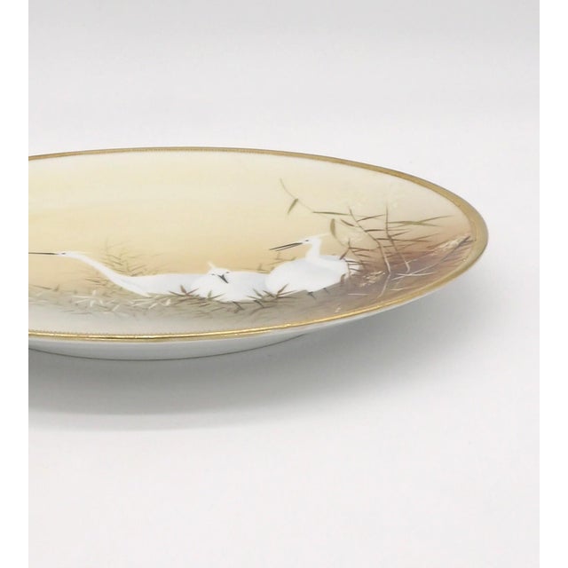 This hand-painted plate features three cranes amid the reeds on a pale yellow background. The plate has an embossed gold...