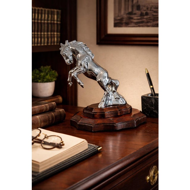A striking vintage chrome rearing horse sculpture, elegantly mounted on a carved wooden base. This sculptural piece evokes...