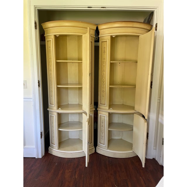 A matched pair of Drexel Heritage Et Cetera corner cabinets in their original cream glaze with hand-painted sepia scroll...