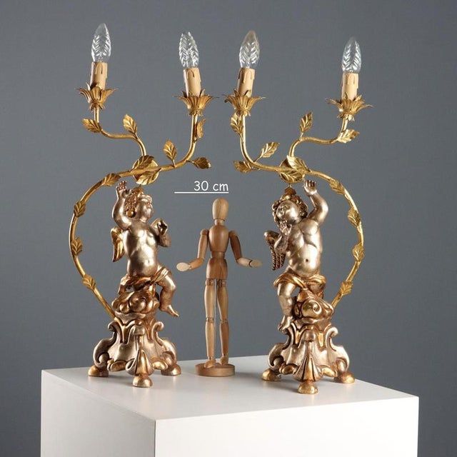 A pair of carved and gilded wooden candelabras. A cherub rests on a triangular base, holding a gilded iron torch holder...