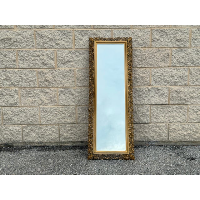 Tall vintage mirror with an ornate molded gilt frame featuring openwork scrolls, lattice details and foliate motifs. Its...