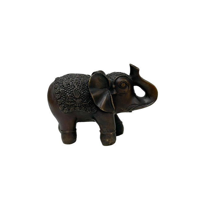 This bronze elephant figurine features a dark, aged patina and intricate decorative details. The elephant is depicted in a...