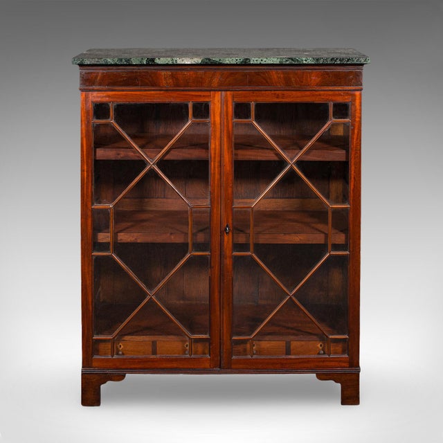 This is an antique astragal glazed bookcase. An English, mahogany and marble display book cabinet, dating to the late...