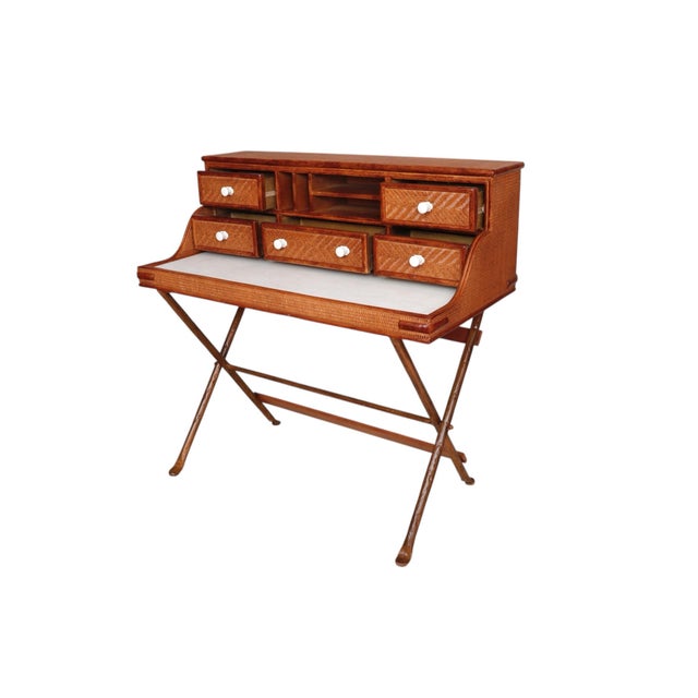 A campaign style writing desk in rattan. The writing area is covered with white faux leather, and the frame is wrapped in...